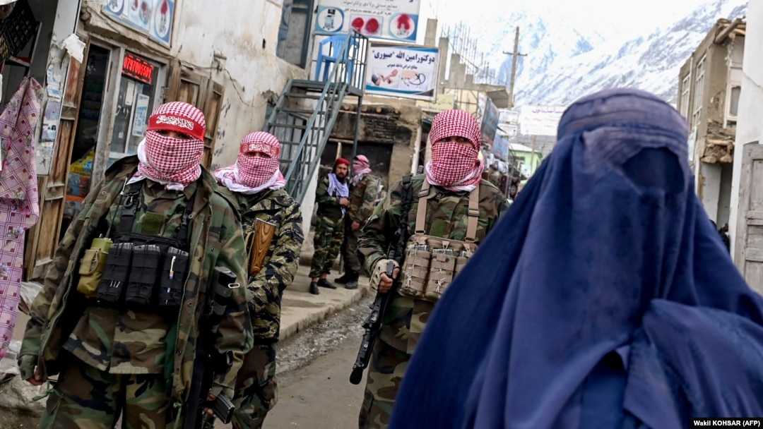 Taliban security personnel patrol a street as a burqa-clad Afghan woman walks by in Badakhshan Province (file photo).