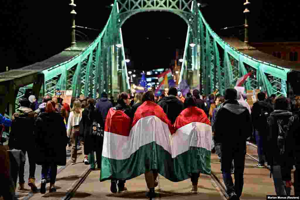 People covered in a Hungarian flag take part in a demonstration in Budapest against a new law banning Pride marches and placing broader restrictions on freedom of assembly in the country.