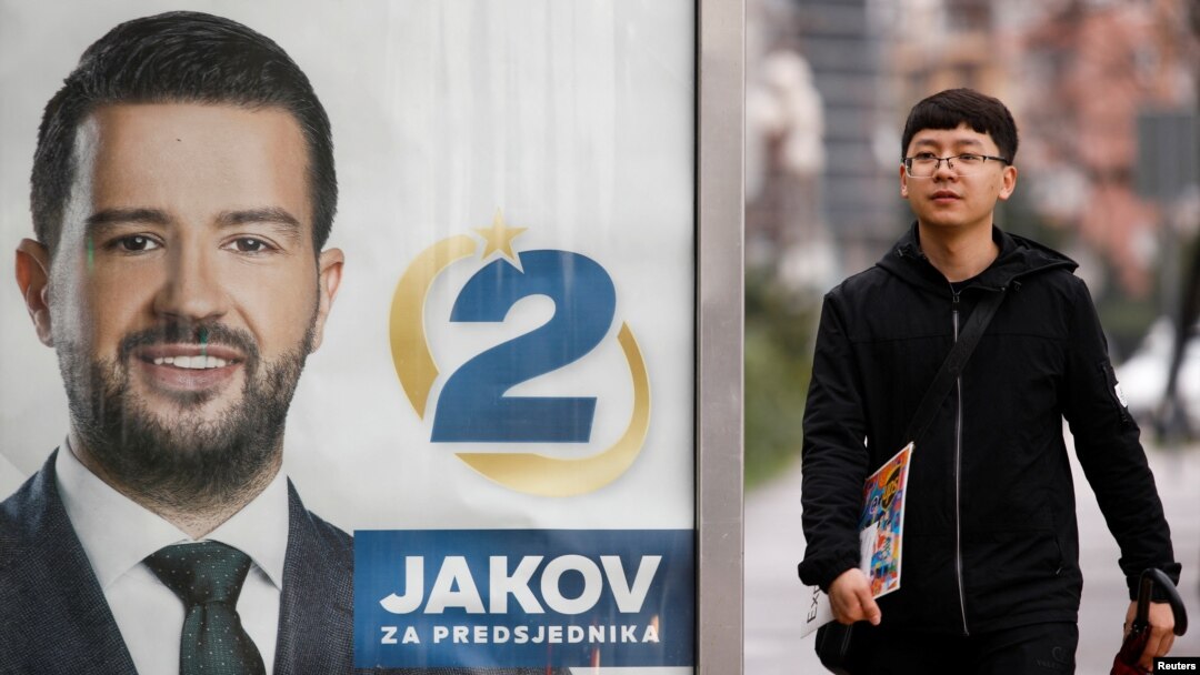 A pedestrian walks past a campaign poster for Jakov Milatovic in Podgoricaahead of the vote.