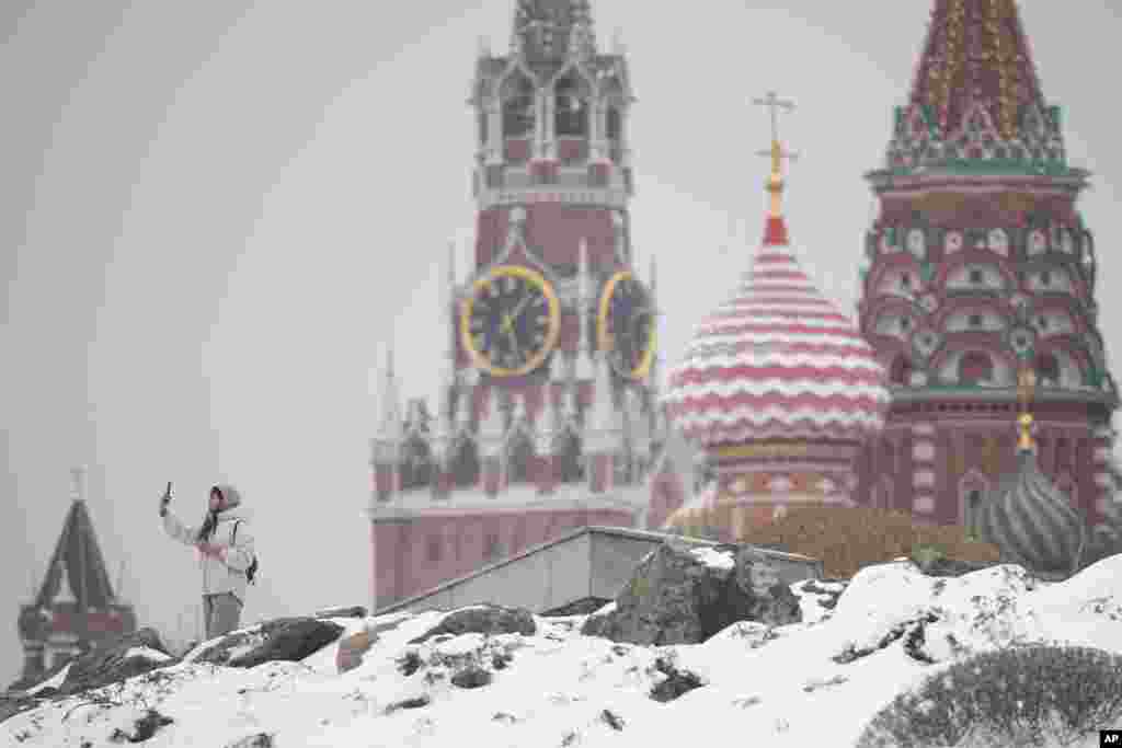 A woman takes selfies in central Moscow with the Kremlin and St. Basil's Cathedral in the background after a snowfall in the Russian capital.