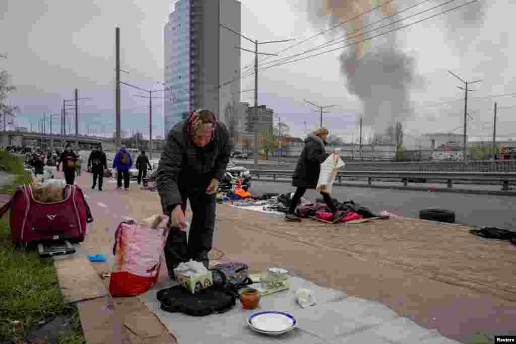 Ukrainian street vendors put their wares on display at a flea market as smoke rises from the nearby site of a Russian missile strike in Kyiv.
