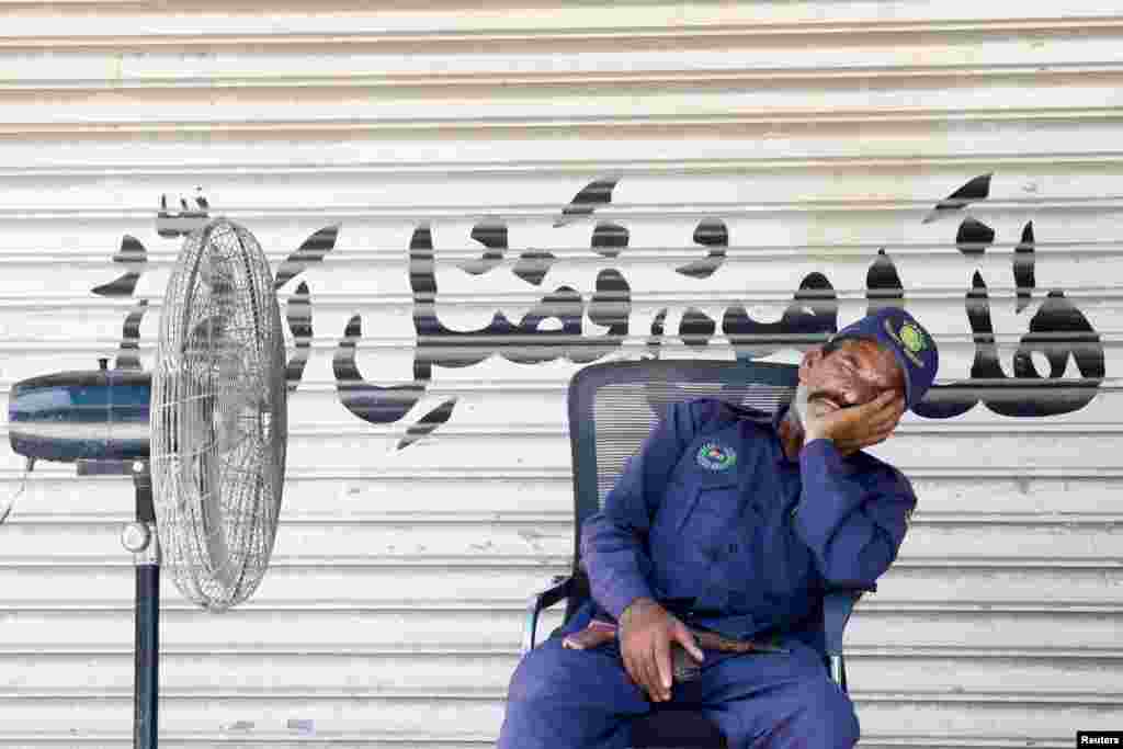 A guard takes a nap beside a fan in front of a closed shop during a hot day in Karachi, Pakistan.