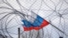 A Russian flag flies behind a fence and barbed wire. (Illustrative photo)