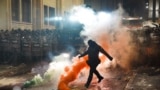 <div>29 лістапада, у другую ноч пратэстаў пасьля абвяшчэньня грузінскім урадам прыпыненьня перамоваў аб уступленьні ў ЭЗ, паліцыянт у масцы падфутбольвае дымавую шашку</div>
