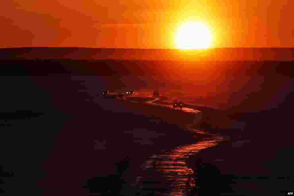 Cars drive along a winter road connecting the banks of the ice-covered Lena River during sunset in Yakutsk, Russia.