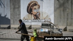 A man pushes his cart past a portrait of late Afghan commander Ahmad Shah Masud that was defaced with spray paint in Kabul.
