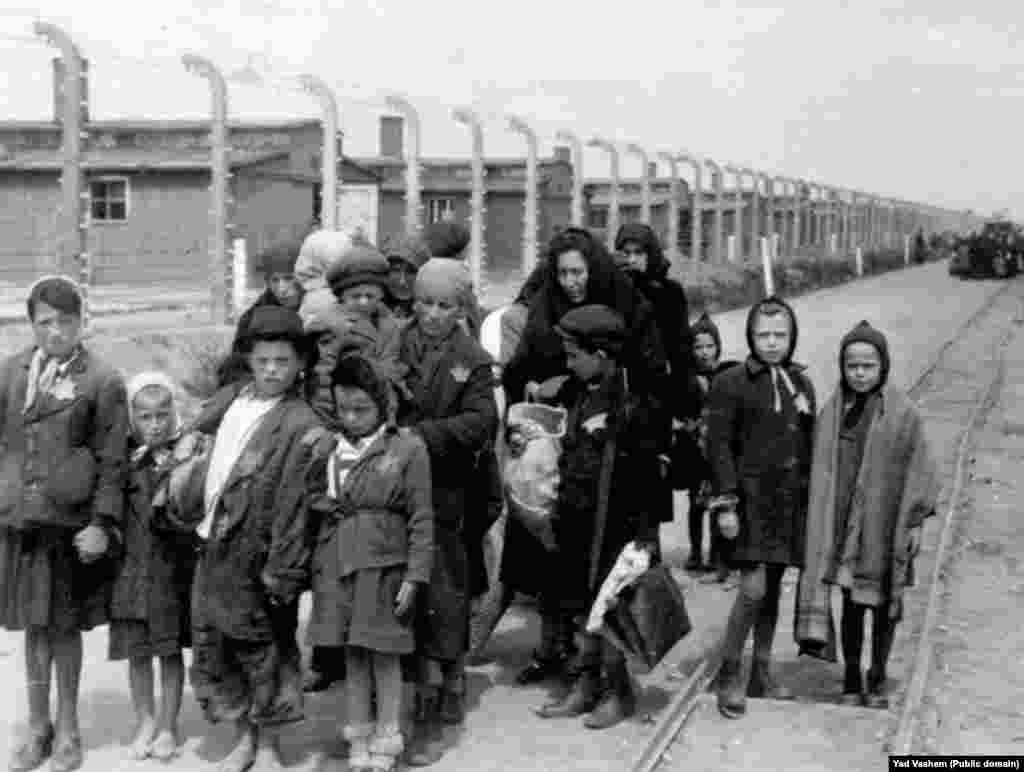 На фото слева: 1944 год. Женщина с детьми направляется в газовую камеру. На заднем фоне видны деревянные бараки – это лагеря Биркенау, дополнительно построенные в Освенциме. После войны здания были разрушены, но кирпичные стены и дымоходы сохранились.