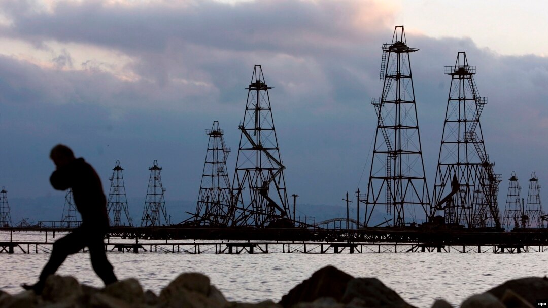 Рабочий на фоне нефтяных вышек на берегу Каспийского моря. 