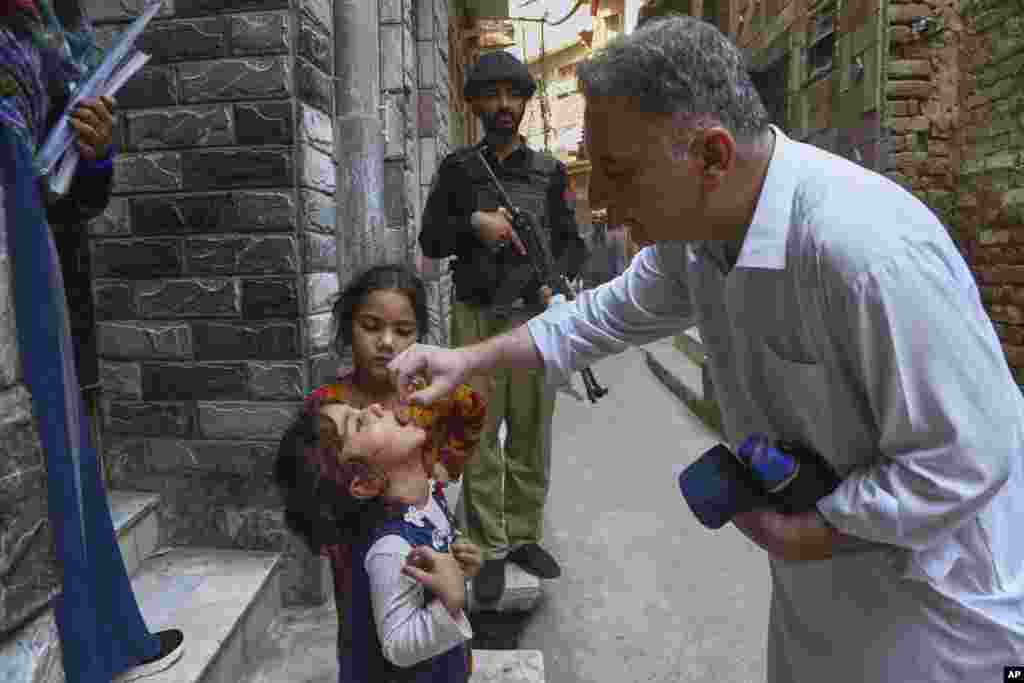 A health worker administers a polio vaccine to a child as a police officer stands guard in a neighborhood in Peshawar in Pakistan's restive Balochistan Province.