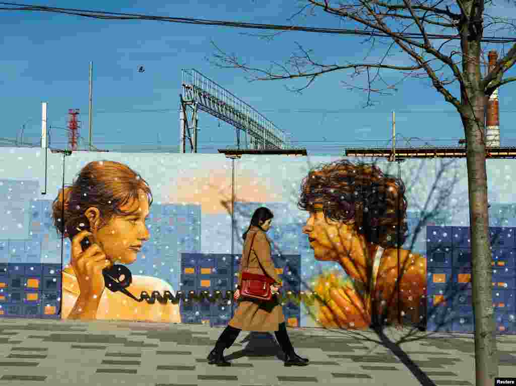 A woman walks past a mural on a street in Moscow.