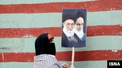 زنی در حال حمل عکس های آیت الله خمینی و خامنه ای در مراسم روز ۱۳ آبان - سالروز اشغال سفارت آمریکا در تهران- که از سوی جمهوری اسلامی «روز ملی مبارزه با استکبار» لقب گرفته است.